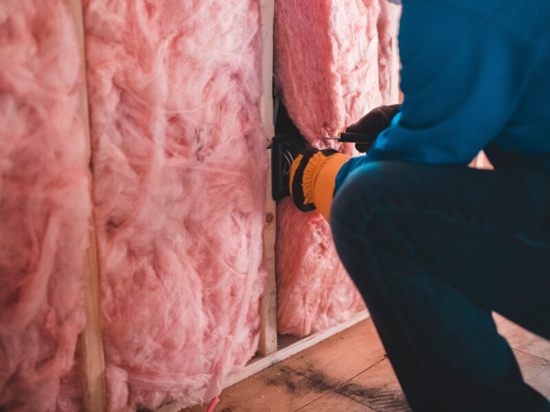 heating and cooling technician installing pink fiberglass insulation in the walls of a home