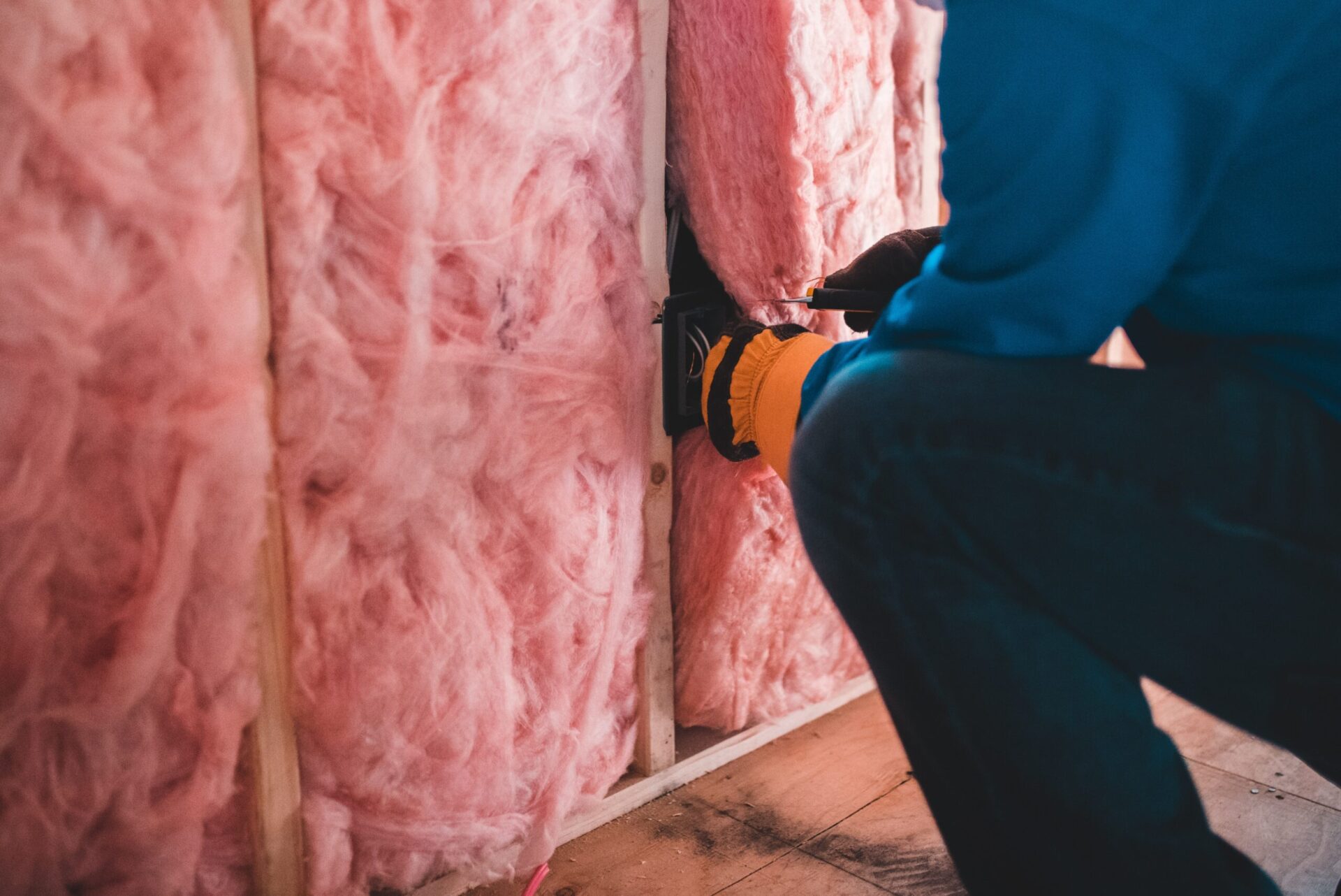 heating and cooling technician installing pink fiberglass insulation in the walls of a home