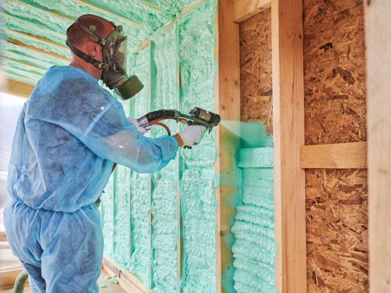 technician in a blue protective suit applying spray foam insulation to a wall