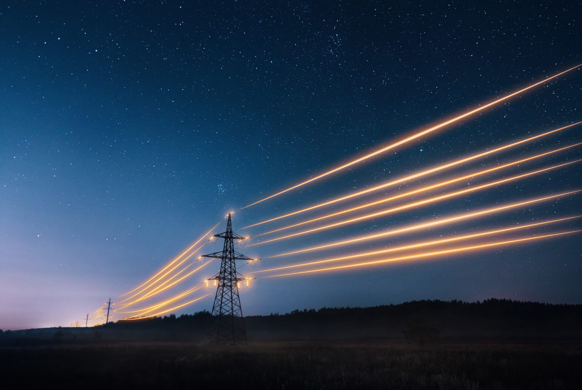 electricity transmission between towers with glowing wires against a nearly dark sky at dusk