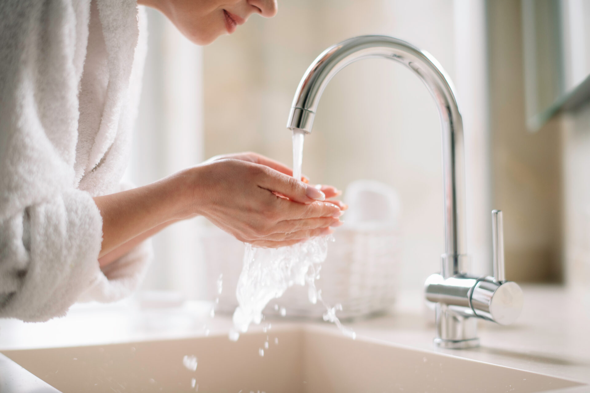 woman in a white robe cupping hot water in her hands from a silver faucet after installing a Bradford white hot water heater